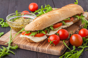 Toasted panini with ham, cheese and arugula sandwich on cutting board