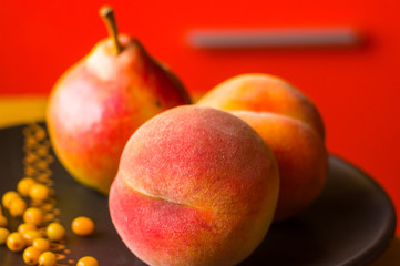 still life - juicy velvety peaches, large ripe pear, and sea buckthorn berries in a ceramic plate on a wooden background