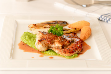 Close up of chicken breast grilled with brown sauce accompanies with white vegetable and crush green peas and potatoes fried, isolated on white plate. 