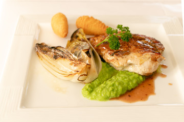 Close up of chicken breast grilled with brown sauce accompanies with white vegetable and crush green peas and potatoes fried, isolated on white plate. 