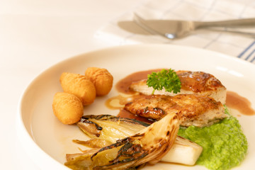 Close up of chicken breast grilled with brown sauce accompanies with white vegetable and crush green peas and potatoes fried, isolated on white plate. 