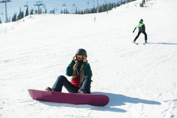 Fototapeta na wymiar Girl with a snowboard sitting on a snowy slope.