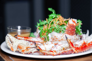 Closeup round white dish with fresh red big boiled prepared blue kamchatka crab with green, sauce. Concept useful seafood in a menu premium restaurant preparing, serving for guests, clients