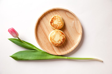 Closeup fresh flower pink tulip on wooden round plate, two golden fried cheesecakes in the shape of a figure 8, dessert made from cottage cheese. Concept tasty and healthy breakfast March 8