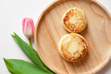 Closeup fresh flower pink tulip on wooden round plate, two golden fried cheesecakes in the shape of a figure 8, dessert made from cottage cheese. Concept tasty and healthy breakfast March 8