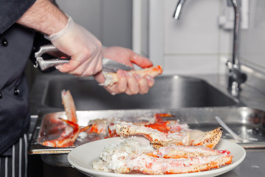 Cook chef is carving fresh red big boiled prepared blue kamchatka crab with scissors. Concept useful seafood in a menu, chef of premium restaurant preparing crab for serving for guests, clients