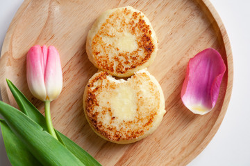 Closeup of fresh pink tulip on wooden round plate, two golden bitten fried cheesecakes in the shape of figure 8, dessert made from cottage cheese. Concept tasty and healthy breakfast March 8