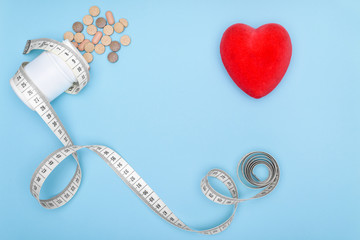 Blue background with heart and copy space.White jar of medications wrapped in a flexible ruler for fitness. The concept of losing weight when taking BIO supplements. Healthy lifestyle.