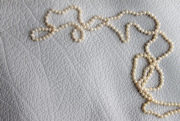 Fototapeta na wymiar pearl necklace on a light leather background top view