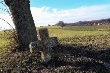 An ancient stone cross under a tree by the road
