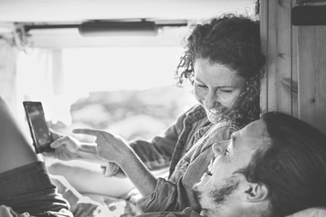 Happy couple watching on their mobile phone in minivan with wood interior - Man and woman using smartphone during their journey - People, technology, social media and youth lifestyle concept