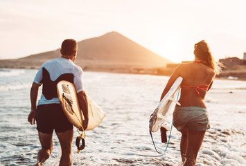 Happy surfer couple running with surfboards along the sea shore - Sporty people having fun going to...