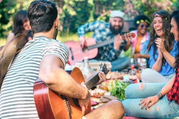 Young people doing picnic and playing guitar in park - Group of happy friends having fun during the...