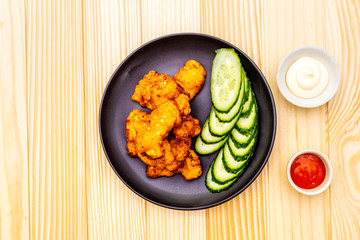Chicken fried (nuggets) homemade on black plate with two sauces - mayonnaise and hot spicy sauce. On wooden background, top view