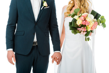 cropped view of bride with beautiful wedding bouquet  holding hands with groom in elegant suit isolated on white
