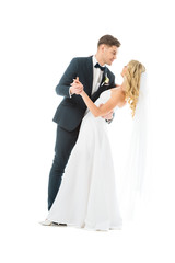 young groom in elegant suit dancing with happy bride isolated on white