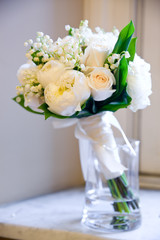 a white bouquet of flowers in a vase of water on a shelf with a shallow depth of field