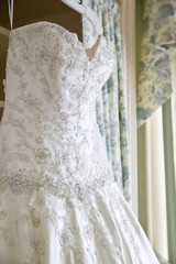 details of a white wedding dress hanging in a room waiting for a bride