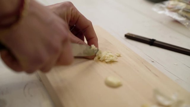close-up of hands chopping garlic on a cutting board
