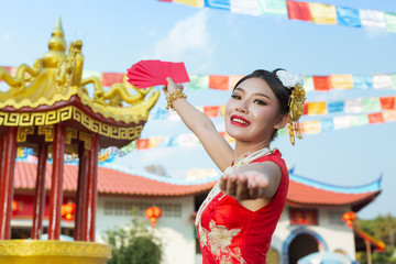 A beautiful asian girl wearing a red dress holding paper fan in her hand and smiling makes her look happy.