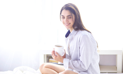 Young beautiful happy brunette woman in black silk dressing gown lying in bed, drinking morning coffee, white cup. Womens day holiday