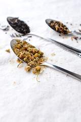 Different types of tea on vintage metal silver spoons on white fabric background with empty copy space. Organic healthy lifestyle and well-being concept. Vintage food and drink setting styling. 