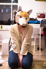 A person kneels on the ground wearing a fox mask carefully made from cardboard cutouts.