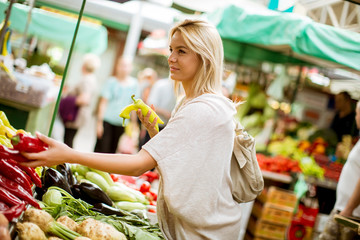Cute young woman buying vegetables at the market