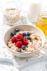 homemade oatmeal with berries for breakfast on white wooden board, vertical closeup