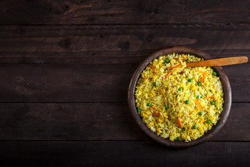 Cooked rice with curry and vegetables in a plate on the wood black background.