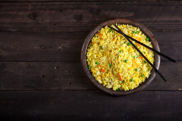 Cooked rice with curry and vegetables in a pan with chopsticks on the wood black background.