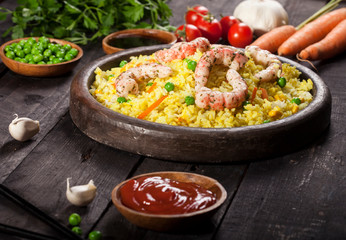 Cooked rice with shrimps, curry and vegetables in a dish on the wood black bamboo background.