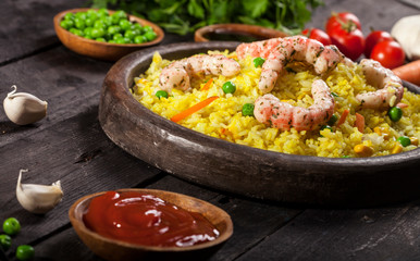 Cooked rice with shrimps, curry and vegetables in a dish on the wood black bamboo background.