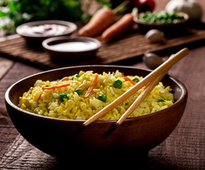 Cooked rice with curry and vegetables in a bowl with sauces and chopsticks on the wood brown background.