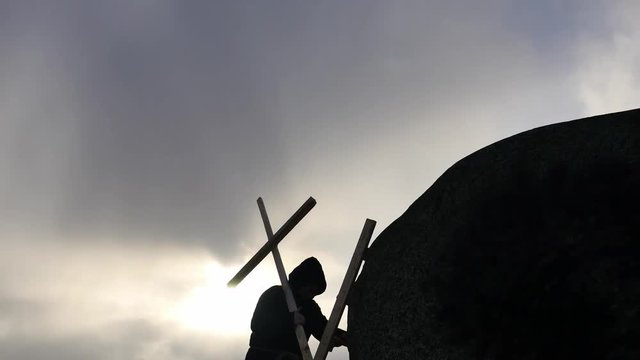 medieval man lifting Christan cross up to the rock top silhouette