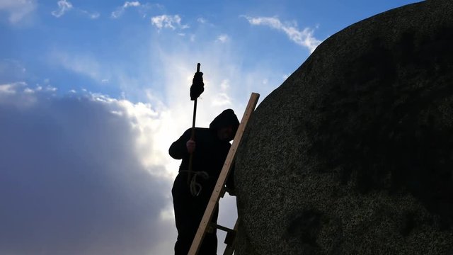 man in hoodie climbing up with burning torch silhouette rock top