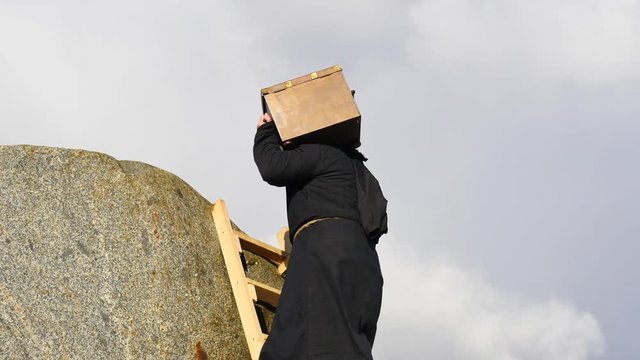 medieval man in hoodie climbing up to high mountains & lifting chest