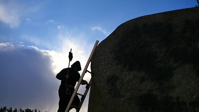 man in hoodie climbing up with burning torch silhouette rock top