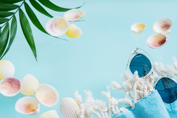 Summer creative concept. Minimal style with transparent glasses, palm leaves, beach towel and seashells on turquoise background with copy space