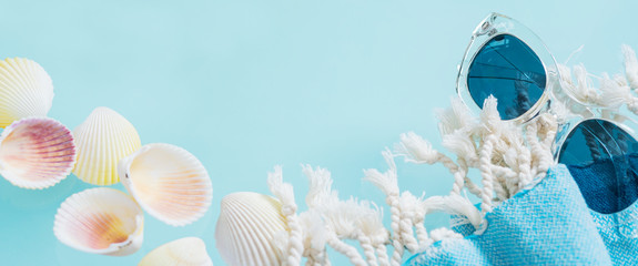 Summer creative concept. Minimal style with transparent glasses, palm leaves, beach towel and seashells on turquoise background with copy space. Long wide banner.