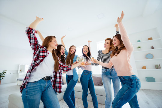 Nice-looking graceful careless carefree charming attractive cheerful cheery positive ladies clinking wine raising hands up vacation in modern light white interior room indoors