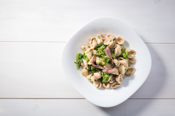 Tipical dish of Apulia region pasta Orecchiette with turnip greens and salted anchovies, top view, white wooden background with copy space
