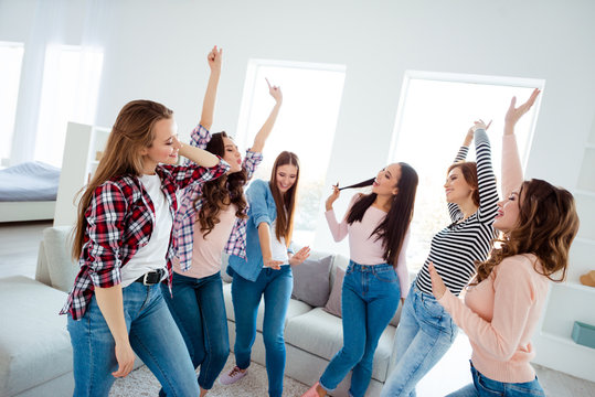 Nice shine graceful charming attractive cheerful cheery glad careless carefree girls wearing trendy casual clothes raising hands up rejoicing in light white interior room house indoors