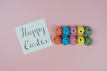 Beautiful painted Easter eggs and greeting card isolated on pink background. Quail eggs. Happy Easter concept. Top view