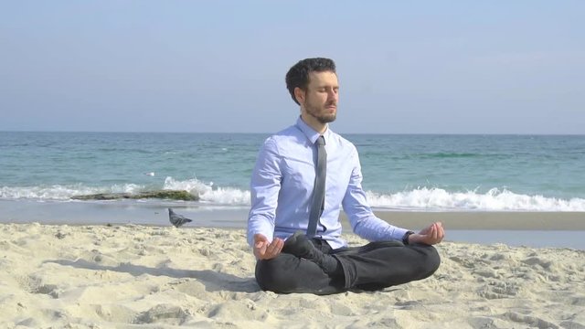 Young male businessman relax on the beach in sunny day an do meditation in  lotus pose 