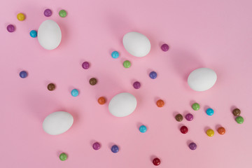 Whole white Easter eggs, multicolored sweets on pink background. Easter decorations, search for sweets for Easter Bunny. Flat lay, top view. Copy Space.