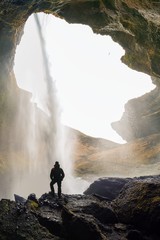 Kvernufoss waterfall at Skogafoss in the gorge of the mountains. Tourist Attractions Iceland. A man in a red jacket stands and looks at the flow of falling water. Beauty in nature background concept