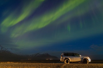 Obraz na płótnie Canvas Aurora borealis above the car. Jokulsarlon glacier lagoon, Iceland. Green northern lights. Starry sky with polar lights. Night winter landscape with aurora. Astronomy background