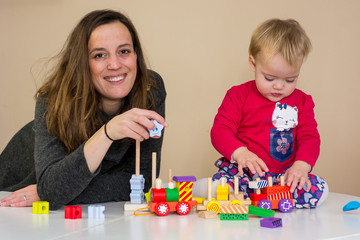 Mother playing with her daughter with wooden toys at the table.