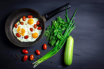 fried eggs with tomatoes in a pan and fresh onions on dark background with space for text. Top view.